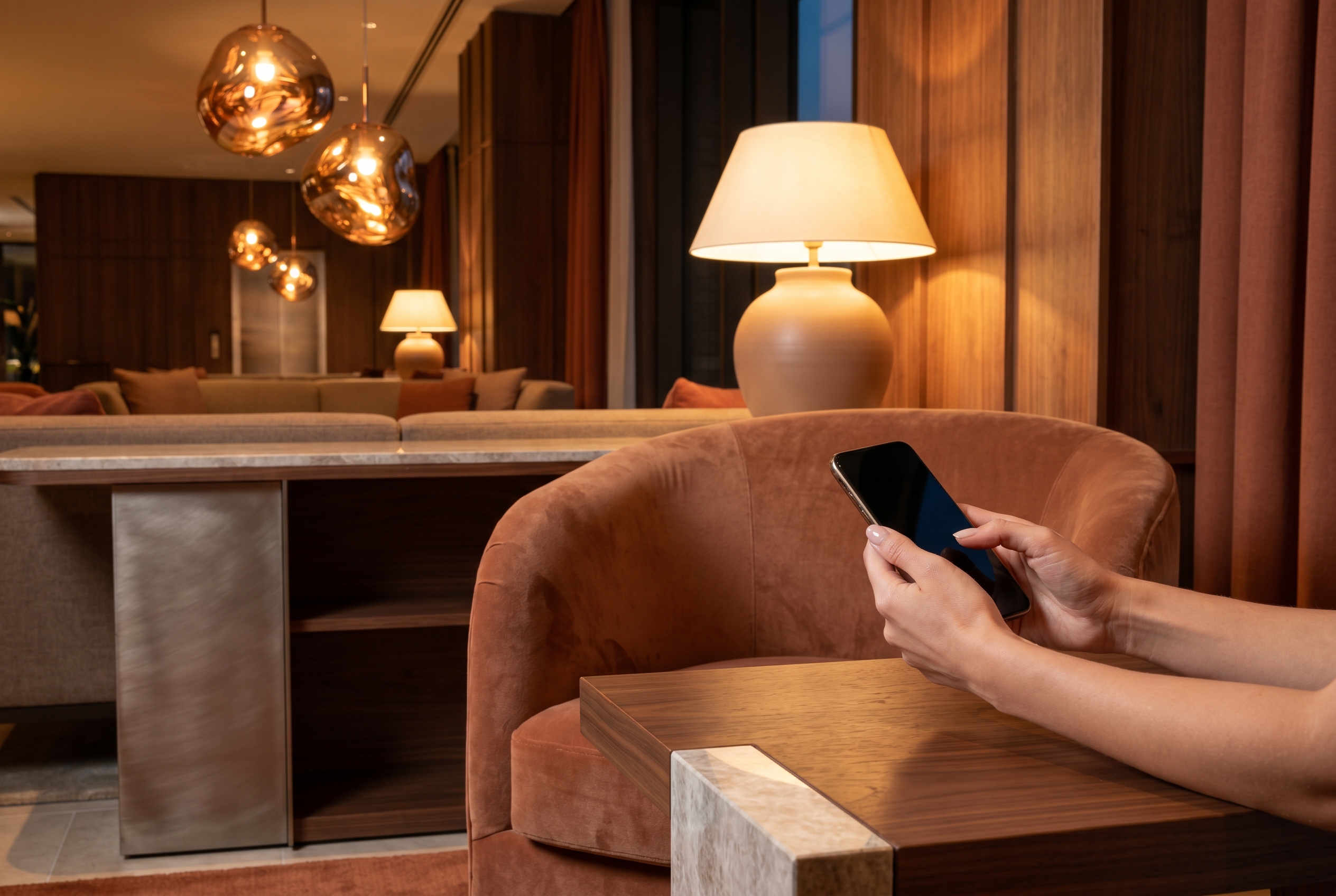 A guest's hands holding a phone in an elegant contemporary hotel lobby lounge at dusk.